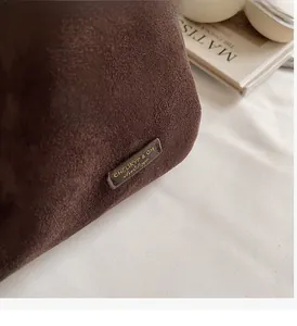 Vue détaillée du sac seau en daim marron foncé avec logo en métal poli et texture rétro
