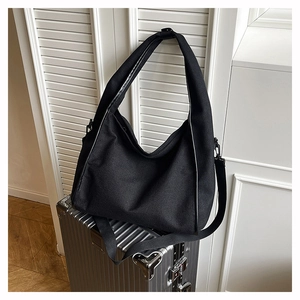 Detail of a black oversized Hobo bag with thick canvas texture on a metallic suitcase