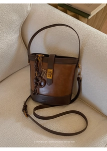 Detail of vintage brown bucket bag with gold twist lock and woven charm on a sofa