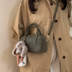 Detail of dark green boston bag with textured finish, gold hardware and rabbit charm