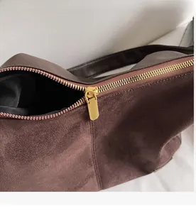 Détail macro d'une fermeture éclair en métal doré lisse sur un sac cabas en daim marron foncé