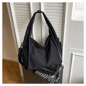 Detail of minimalist black canvas hobo bag with adjustable strap on silver suitcase