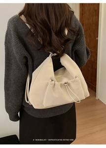 Close-up of beige minimalist hobo bag with drawstring pocket detail on a model back