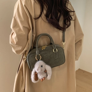 Close-up of olive green vintage pillow bag with plush rabbit charm and gold zippers