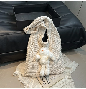 Detail of a beige knitted tote bag with a cute white bunny plush on a textured grid surface