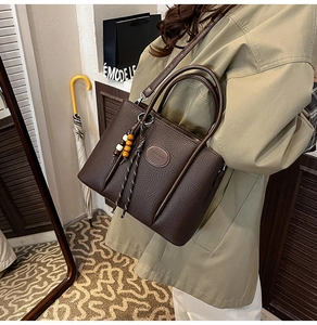 Detail showing dark brown litchi grain leather bucket bag with colorful wood bead charm