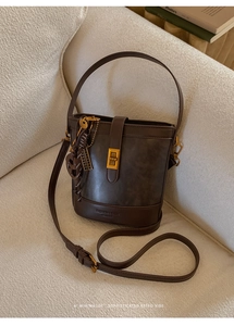 Close-up of matte brown leather bucket bag with embossed logo and golden square buckle