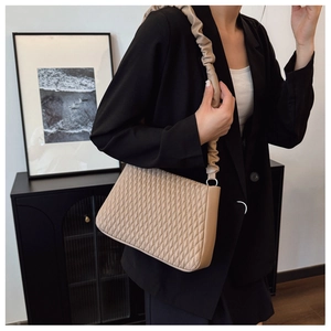 Chic quilted shoulder bag with ruched strap styled with a black blazer in a modern interior
