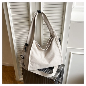 Detail of beige canvas hobo bag with wide strap hanging over a silver suitcase