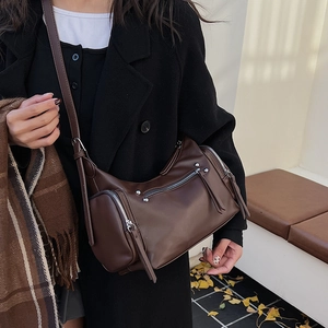 Detail of dark brown leather crossbody bag with silver zippers and stud accents