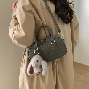 Detail view of dark olive Boston bag with plush bunny charm on khaki trench coat