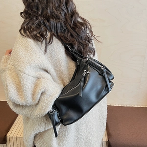Detail of a black cylinder crossbody bag with silver zippers shown on a model