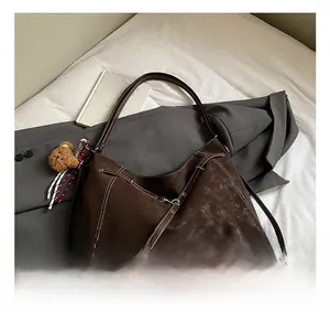 Close-up of brown suede tote bag featuring white contrast stitching and bear charm