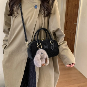Detail of black suede Boston bag with golden hardware and plush bunny charm on a model