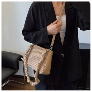 Detail of beige quilted shoulder bag with decorative pleated strap on female model