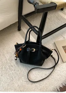 Gros plan du sac cabas noir mat avec boucle dorée et breloque en perles sur tapis doux