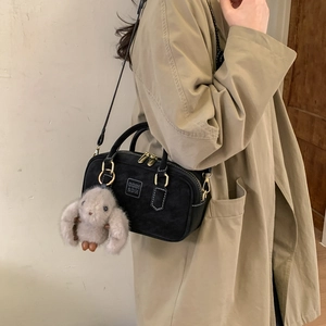 Detail of black suede-textured crossbody bag with golden hardware and a grey bunny charm