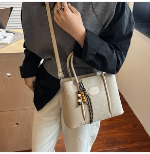 Detail of beige lychee leather bucket bag with top handle and wooden bead accessory