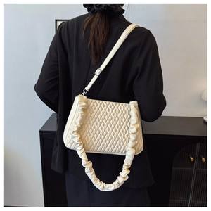 Detail of a beige quilted shoulder bag with a stylish ruched strap shown on a model