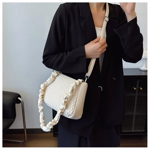 Detail of quilted rhombic texture and ruffled shoulder strap on a beige underarm bag