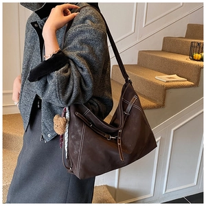 Detail of a large brown suede tote bag with white contrast stitching and a bear pendant