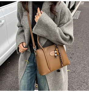 Close-up of brown litchi pattern leather handbag with wooden bead charm and long strap