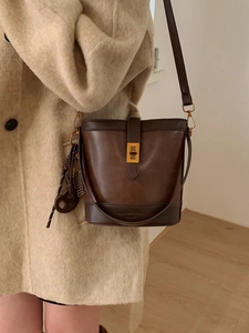 Retro dark brown leather bucket bag with gold clasp shown on model in cream coat