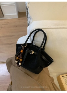 Detail of black suede tote bag with retro metal buckle and decorative beaded keychain charm