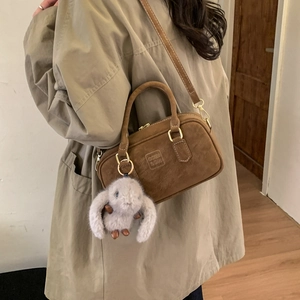 Detail of a brown suede Boston bag with a plush rabbit charm and crossbody strap