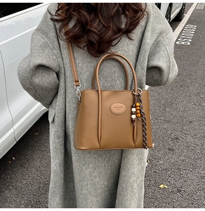 Brown lychee leather bucket bag with wooden bead tassel shown in outdoor lifestyle setting