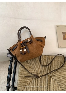 Detail of a brown suede tote bag with leather handles and decorative wooden beads