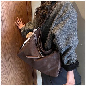 Close-up of vintage brown tote with contrast stitching and fuzzy ball charm on grey coat