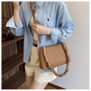 Caramel brown quilted underarm bag with pleated strap shown on a blue plaid shirt