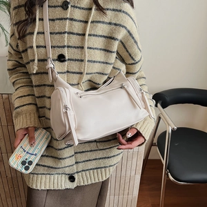 Detailed view of cream PU leather shoulder bag with zipper pockets worn by a model