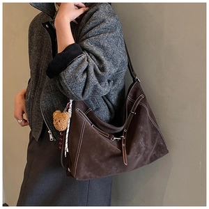 Detail of deep brown suede hobo bag with contrast stitching and bear charm