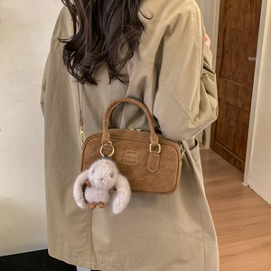 Close-up of retro brown Boston bag in matte suede with plush bunny charm and shoulder strap