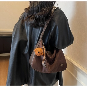 Dettaglio di una borsa hobo in camoscio marrone con ciondolo a orsetto e nappa intrecciata