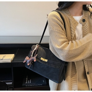 Detail of a black tote bag featuring a golden twist lock and a dachshund bag charm