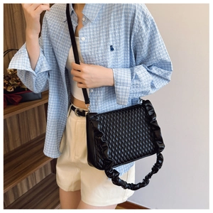Detail of black quilted shoulder bag with ruffle trim and pleated handle on a model