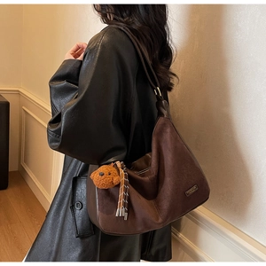 Dettaglio di una borsa Hobo marrone con trama scamosciata, logo metallico e ciondolo a orsetto
