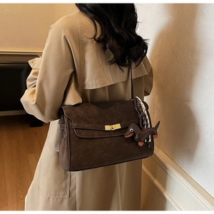 Detail of dark brown suede tote bag featuring a gold buckle and dog-shaped leather charm