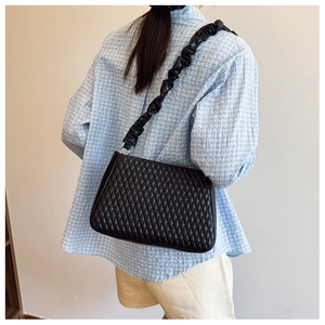 Close-up of black quilted shoulder bag featuring stylish ruched strap on model shoulder