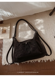 Close-up of retro black suede hobo bag with drawstring pocket on white fringe rug