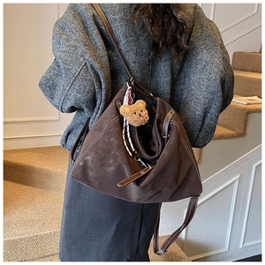 Close-up of brown suede tote bag with contrast stitching and decorative bear charm