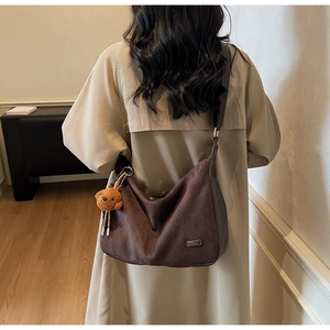 Dettaglio borsa hobo in camoscio marrone scuro con tracolla larga e ciondolo orso