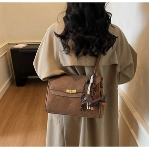 Detail of brown matte leather tote bag with gold buckle and dog charm on a beige coat