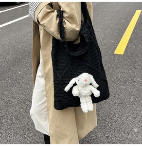 Detail of black crochet tote bag with a white plush bunny charm on a casual outfit