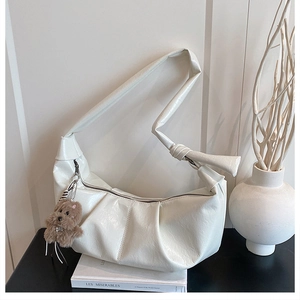 Detail of white pleated crescent bag with knot strap and plush puppy charm on books