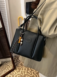 Black pebbled leather bucket bag with colorful beaded charm on a model in trench coat