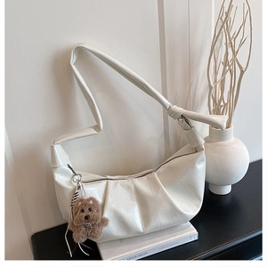 Detail of white glossy pleated hobo bag with a decorative brown plush bear charm accessory